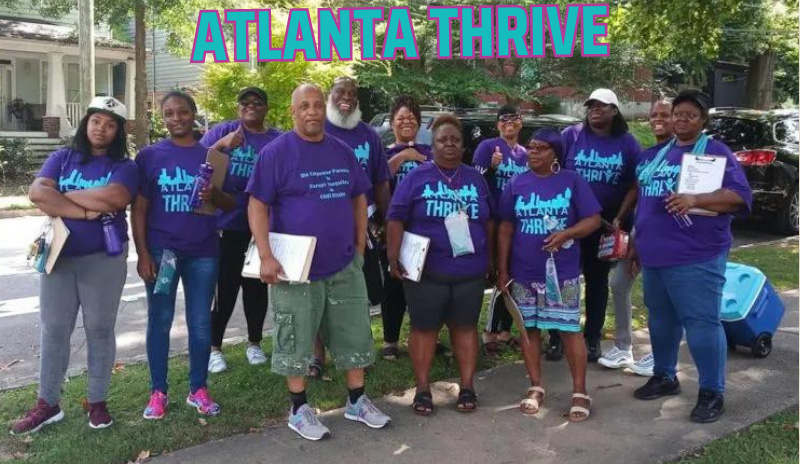 Photo of a group of people of color facing the camera, outdoors, wearing matching shirts that say "Thrive" and with the text "Atlanta Thrive" overlaid at the top. 