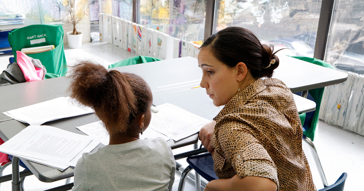 A teacher sits with a student one-on-one in a classroom