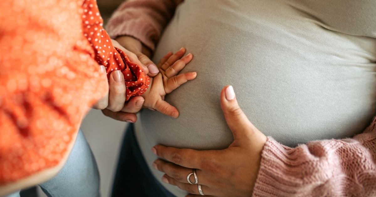 A child putting their hand on their pregnant mother's belly