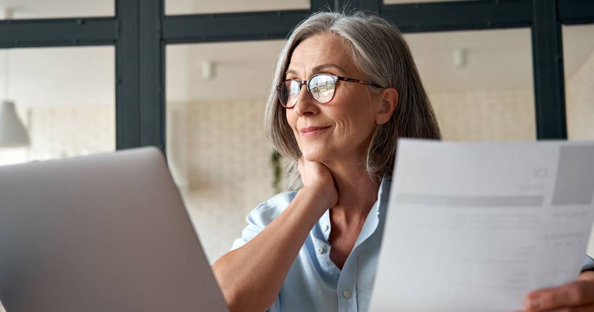 A smiling senior woman reviewing a health care bill and sitting at her laptop