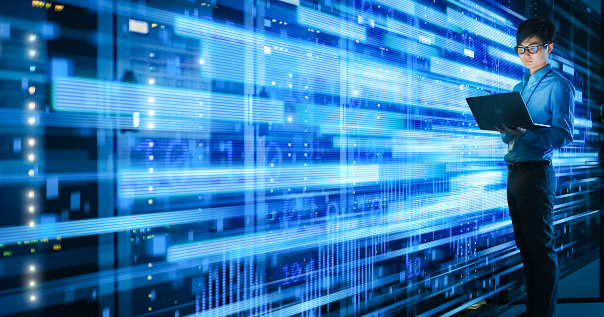 A person stands in a server room, engrossed in a laptop. Blue light trails and data patterns emphasize technology and focus, creating a futuristic tone.