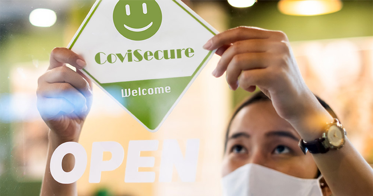 A worker wearing a face mask hangs a sign in a window reading "Covisecure: Welcome" above the word "OPEN". 