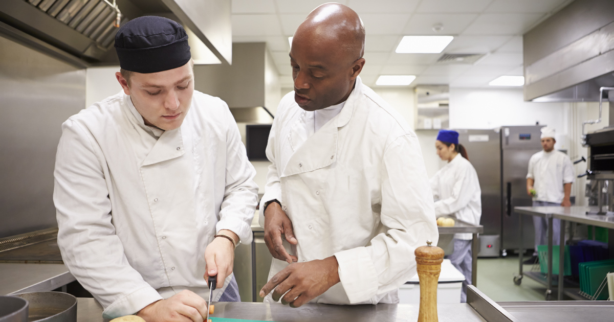 A chef trains a man in a commercial kitchen.