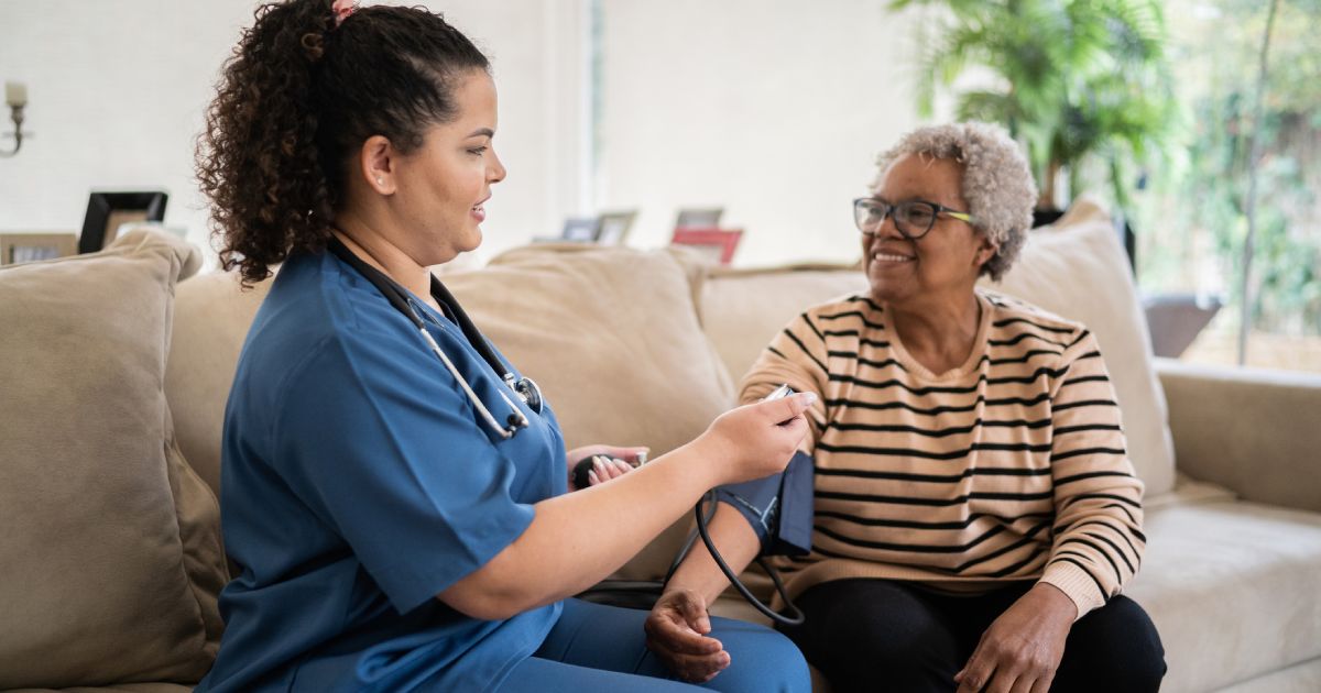 Healthcare worker taking blood pressure of senior woman at home