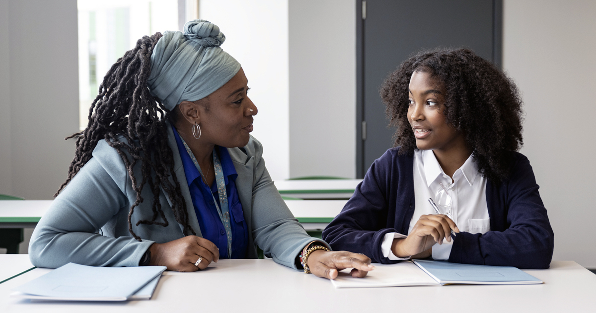A Black educator works with multiracial student in a classroom.