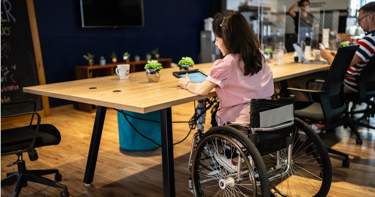 Woman with a disability sitting at a community office table in a wheelchair looking at a tablet