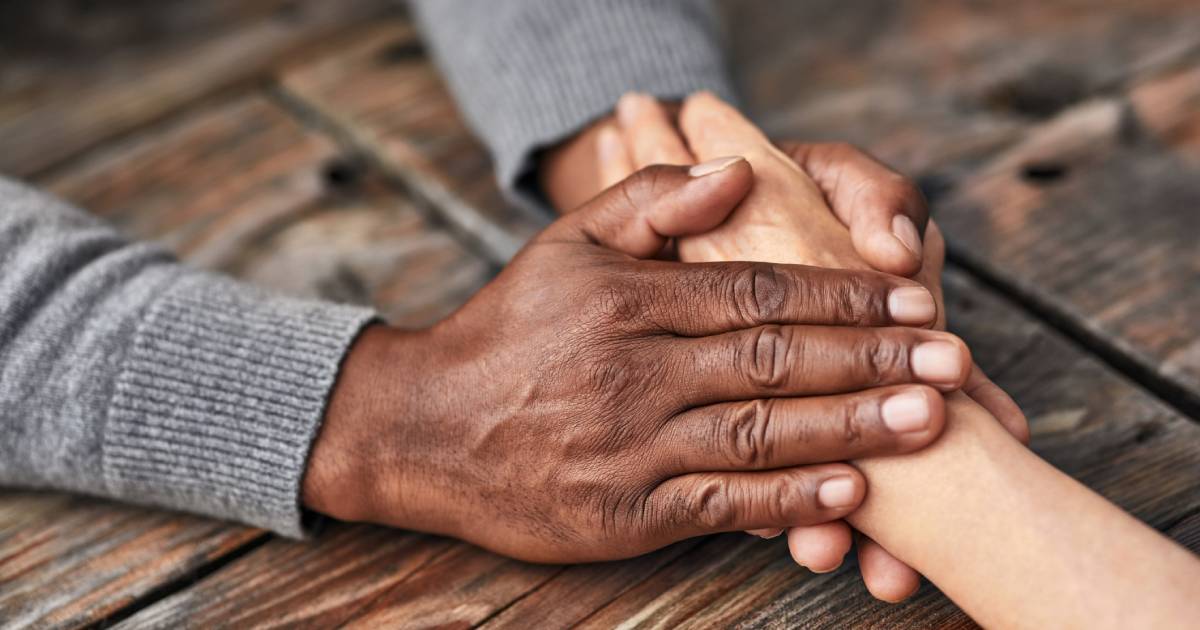 A close up of a caregiver and patient holding hands