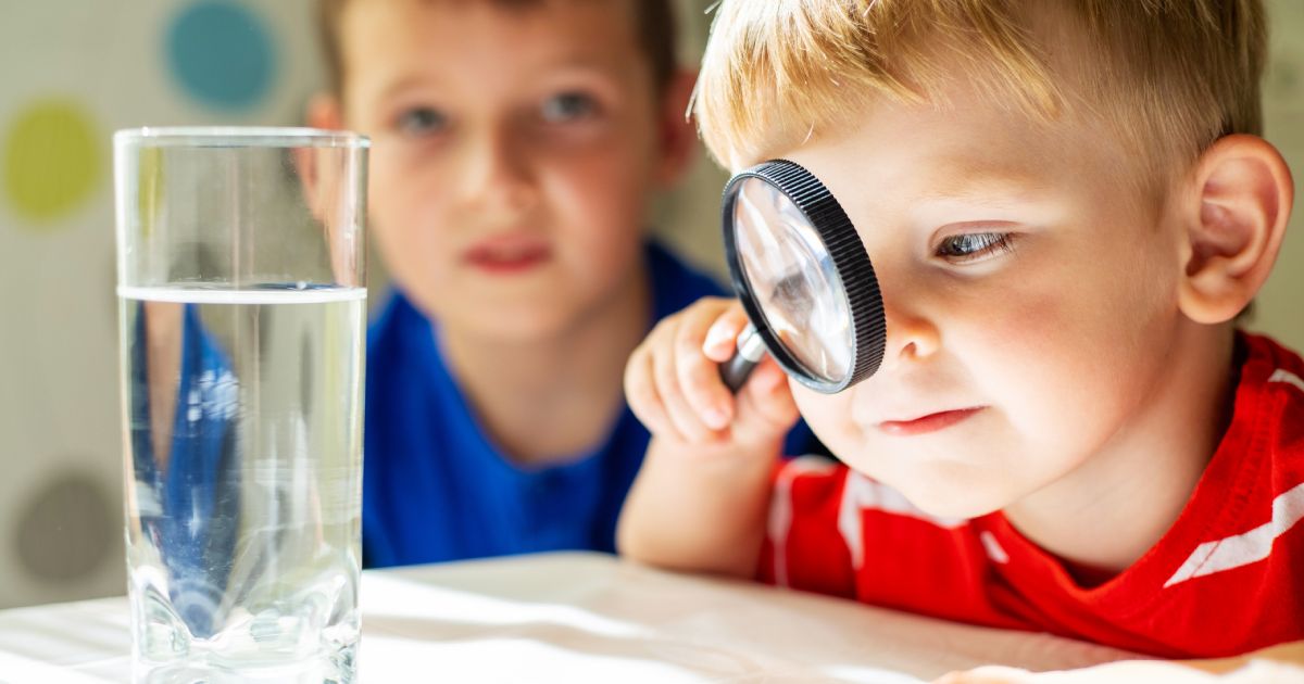 a child looking at water in a glass through magnifying glass