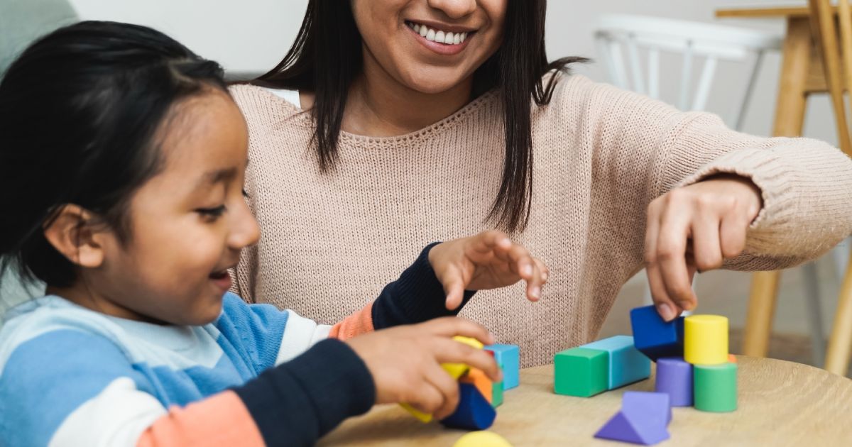 Latin American mother and child having fun playing games with wood toy bricks at home - Family time together